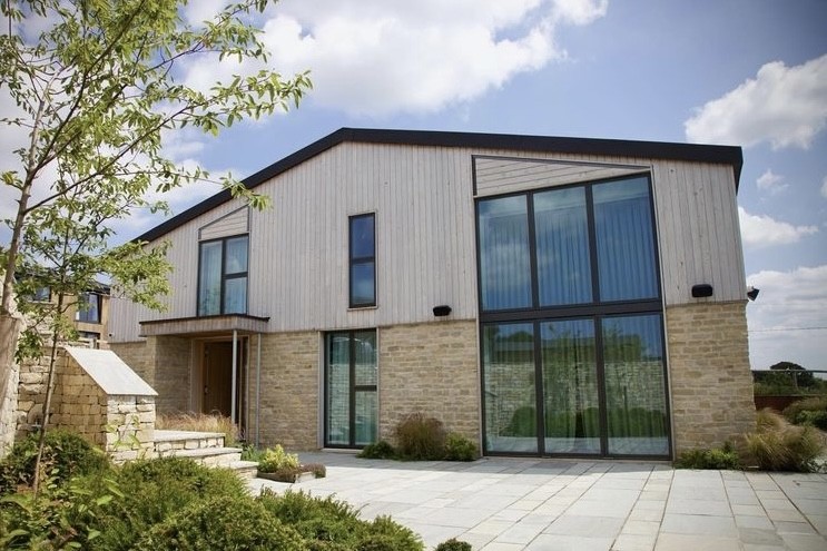 Completed low energy home with timber cladding, a stone base and full-height glazing