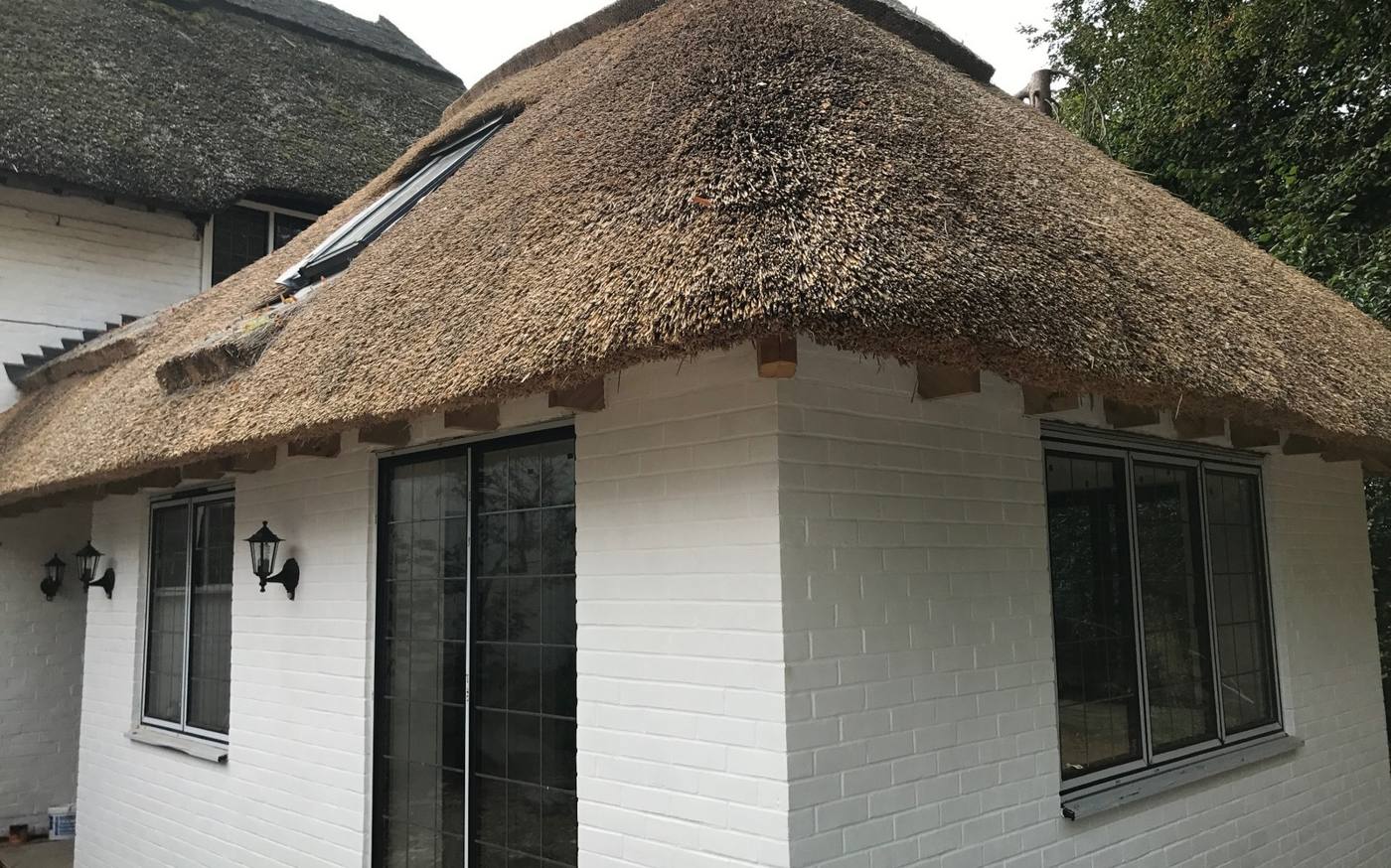 White brick extension beneath a new thatched roof with glazed doors