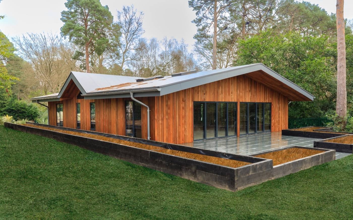 Timber-clad pavilion with a wide overhanging roof in a wooded garden