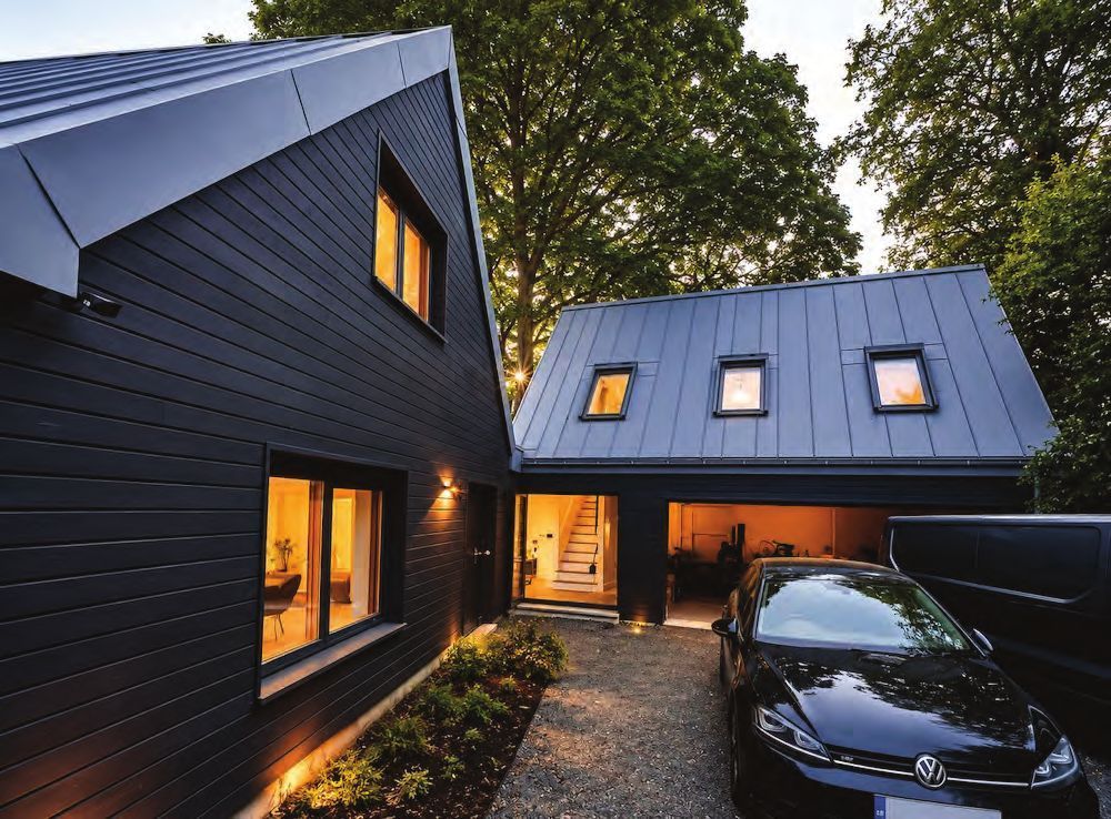 Completed dark-clad hybrid home with a zinc roof in Greater London, lit at dusk