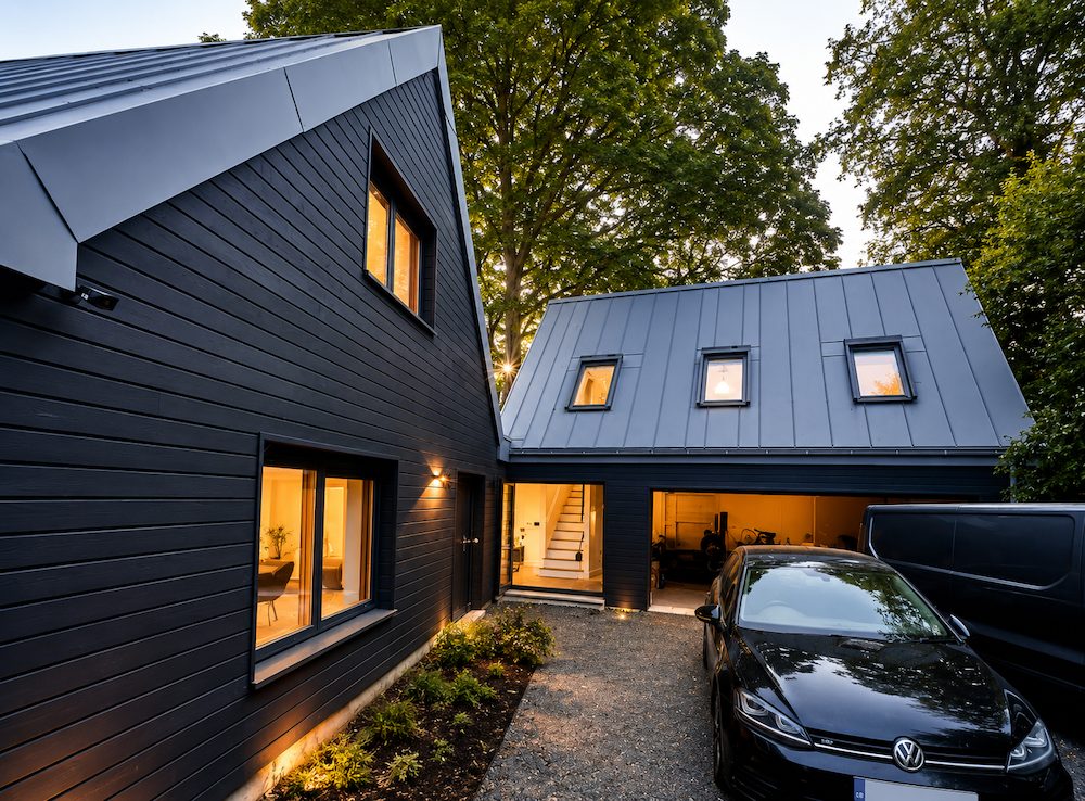 Charcoal-clad low energy home with zinc roof and garage studio, lit at dusk